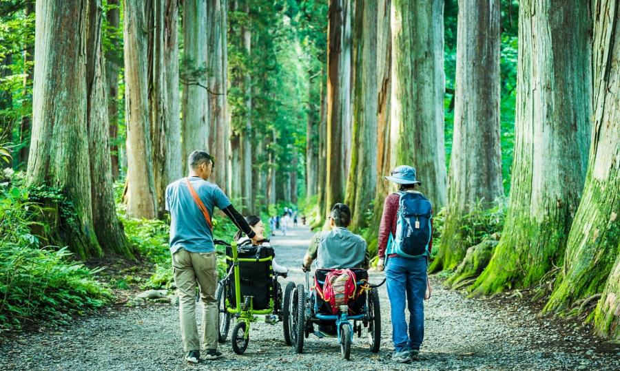 森林の中を散策する車いすの人と徒歩の人