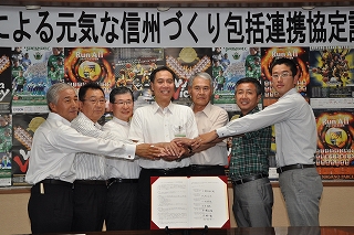 写真：調印した写真を前に握手を交わす7団体の代表者