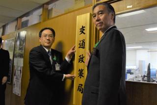 交通政策局の看板を持つ知事と小林局長