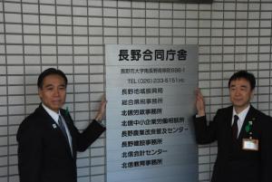 写真：地域振興局の看板の前で記念撮影する知事と長野振興局長